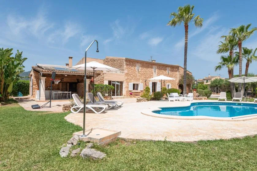 An outdoor swimming pool beside a stone building, with lounge seating and palm trees.