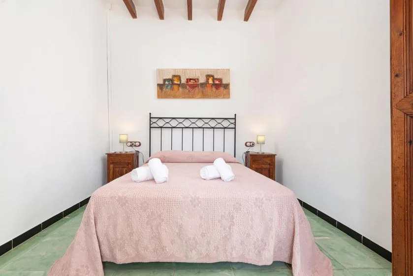 A bedroom with a pink-covered bed, bedside tables, and exposed ceiling beams.