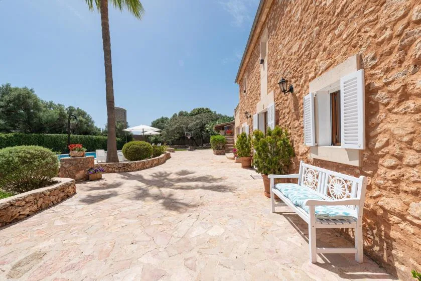 A sunlit stone-paved courtyard runs alongside a rustic stone building with a bench.