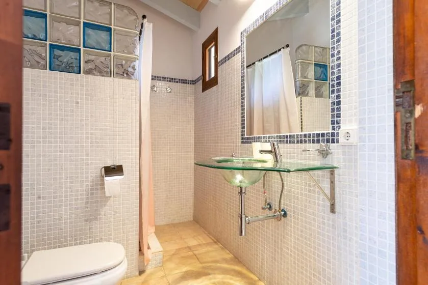 A tiled bathroom with a glass sink shelf, mirror, shower curtain, and toilet.