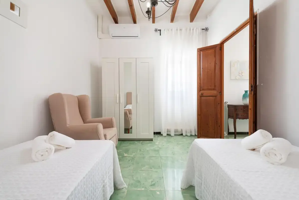 A bright bedroom with two beds, a wardrobe, and a wooden doorway.