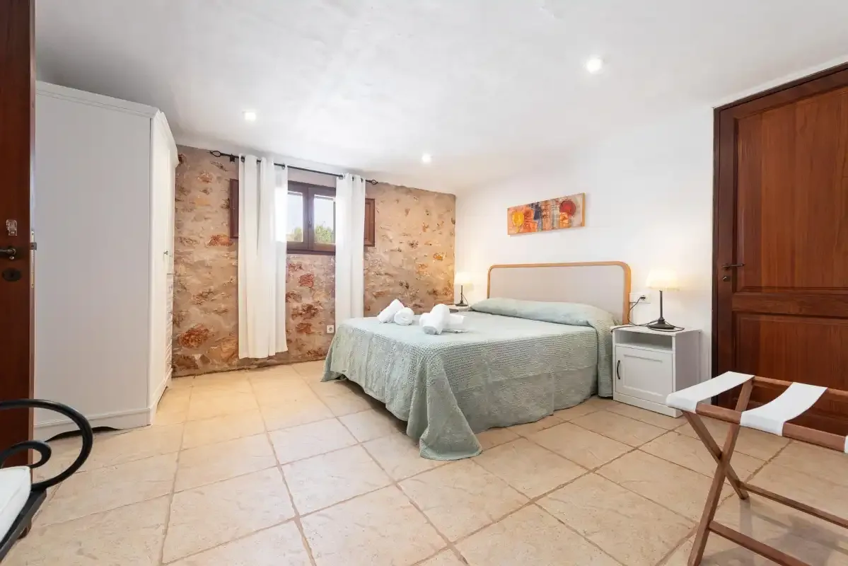 A bedroom with a bed, bedside table, and a window set in an exposed stone wall.