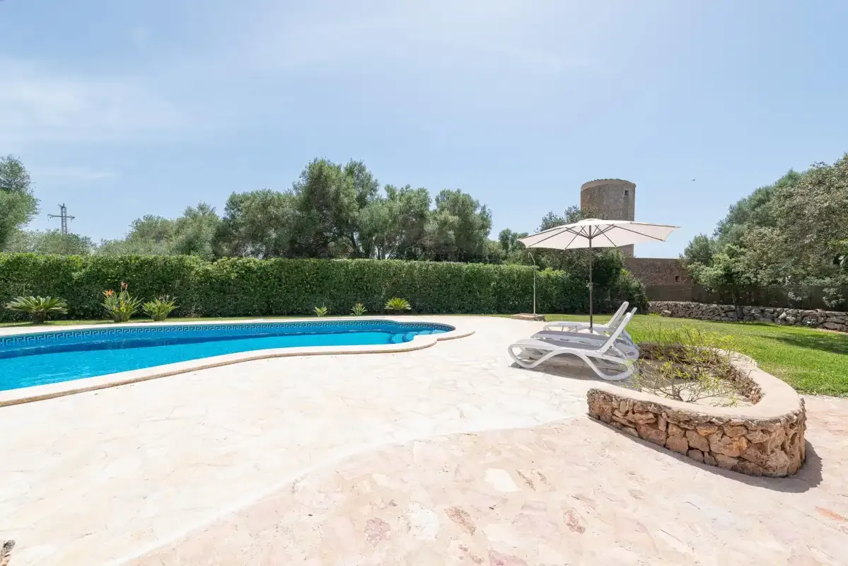 An outdoor swimming pool sits beside a paved patio with a sun umbrella.