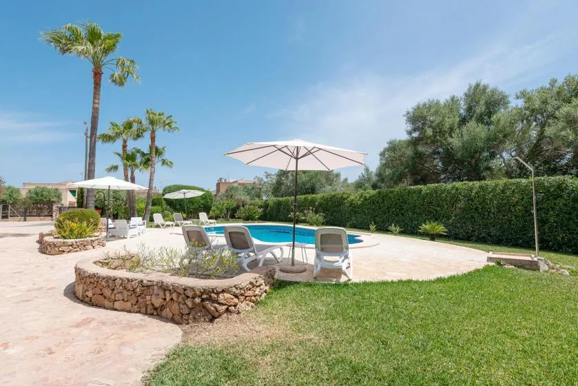 An outdoor swimming pool is surrounded by sun loungers, umbrellas, and green landscaping.