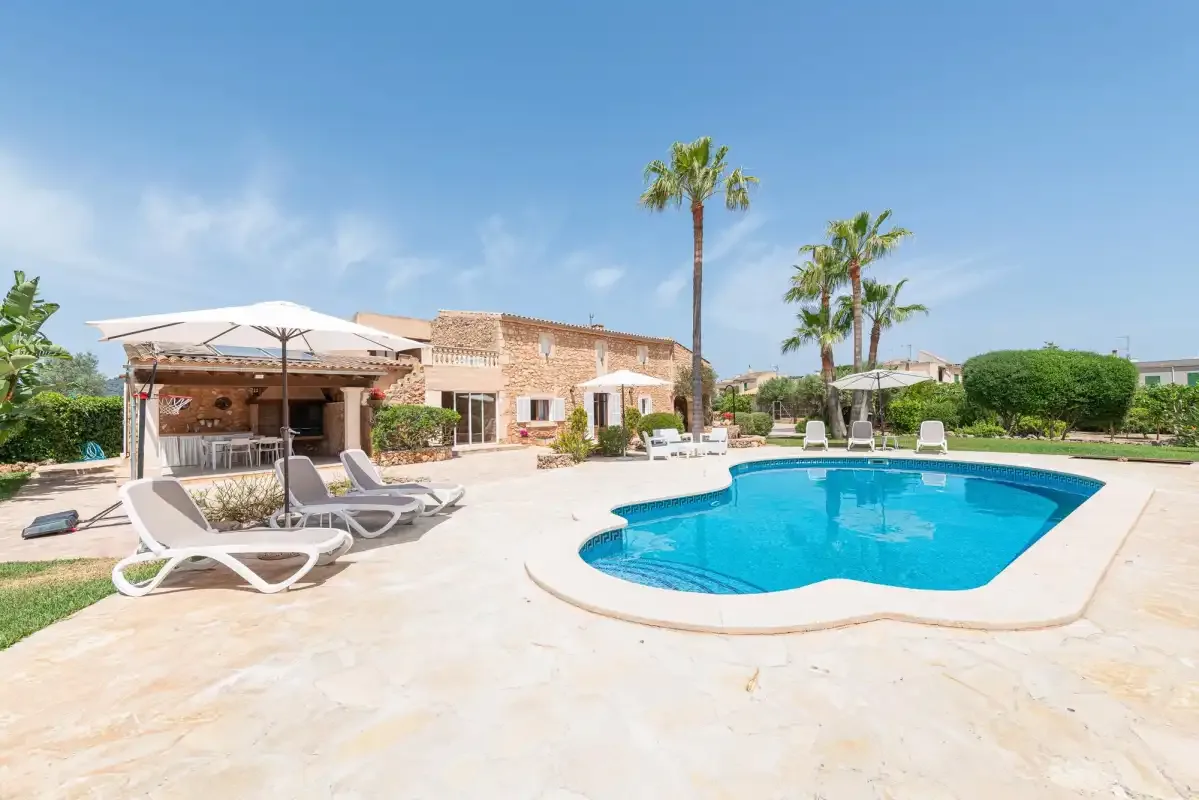A swimming pool beside a patio with loungers and a low stone building.