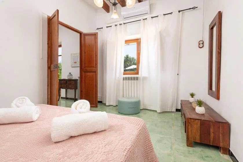 A bedroom with a bed, white curtains, and a small cushioned seat by the window.