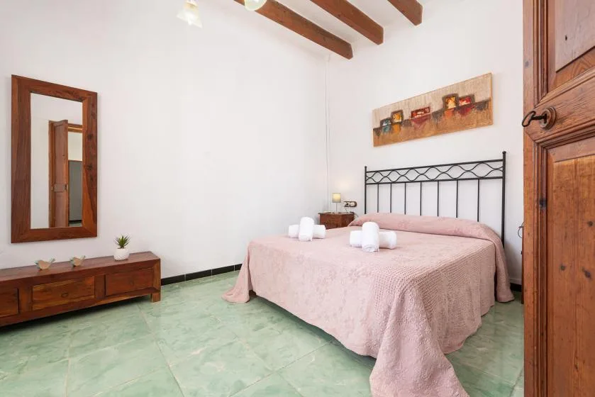 A bedroom with a double bed covered in pink bedding and a wooden dresser.