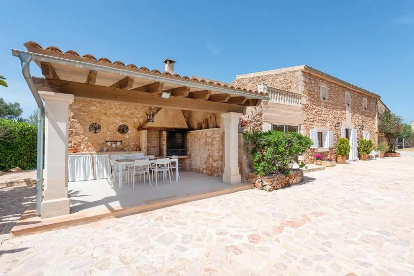 A stone house with a covered outdoor dining area opening onto a sunny paved courtyard.