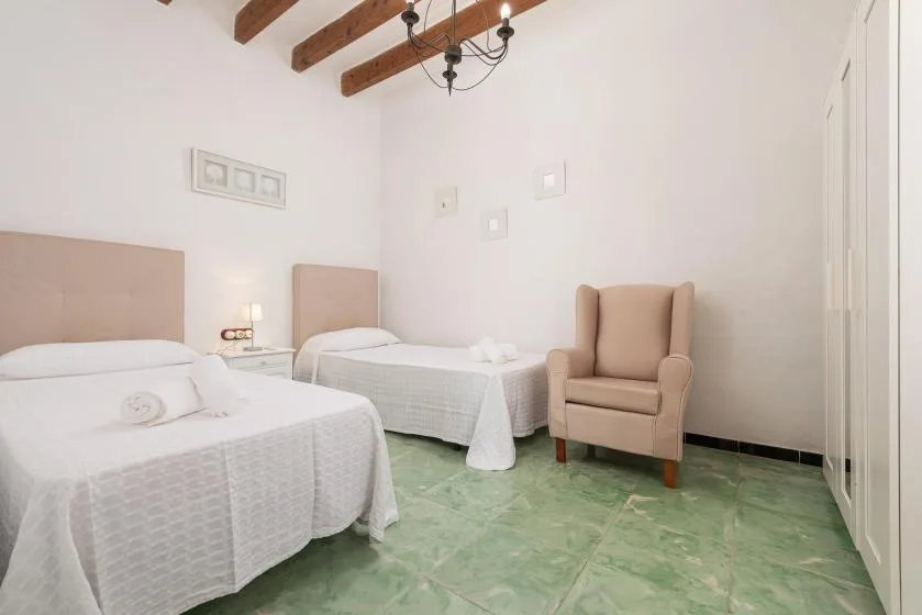 A bedroom with two beds, a chair, and green tile flooring.