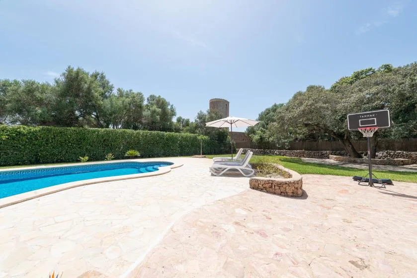 An outdoor pool area with lounge seating and a basketball hoop.