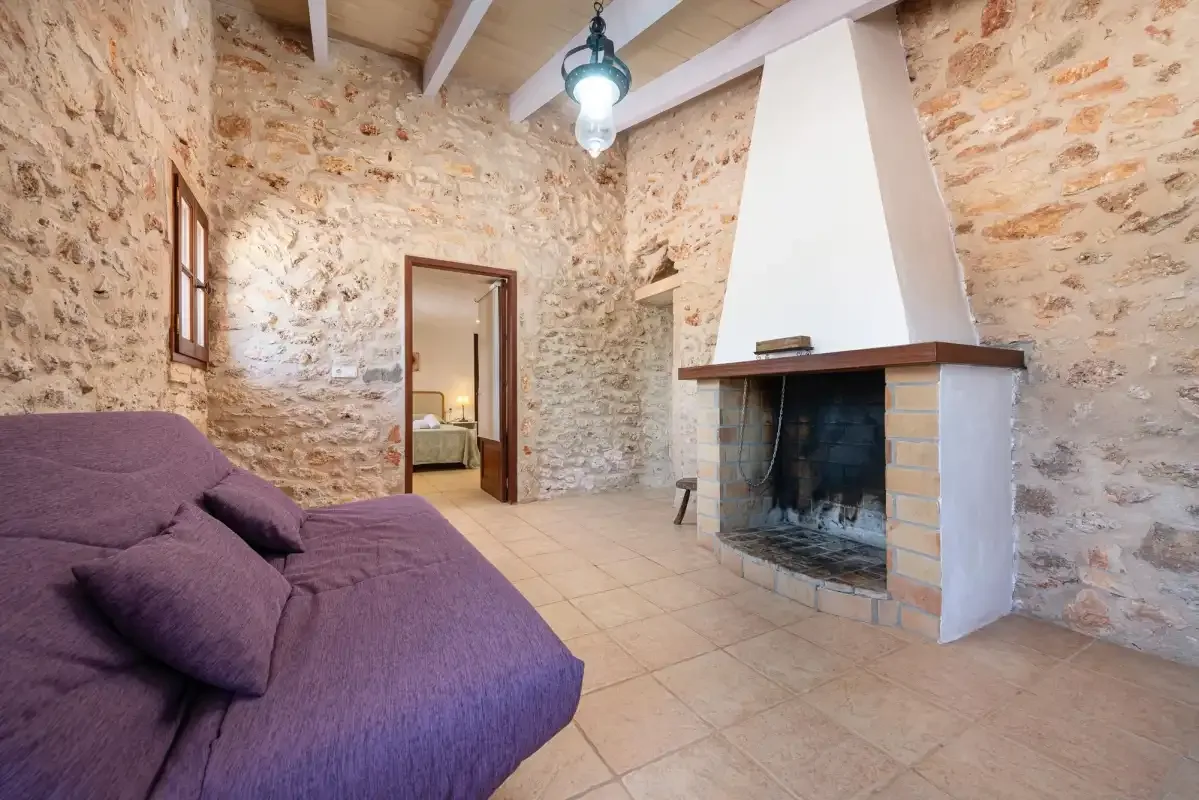 A stone-walled living room with purple seating and a large fireplace.