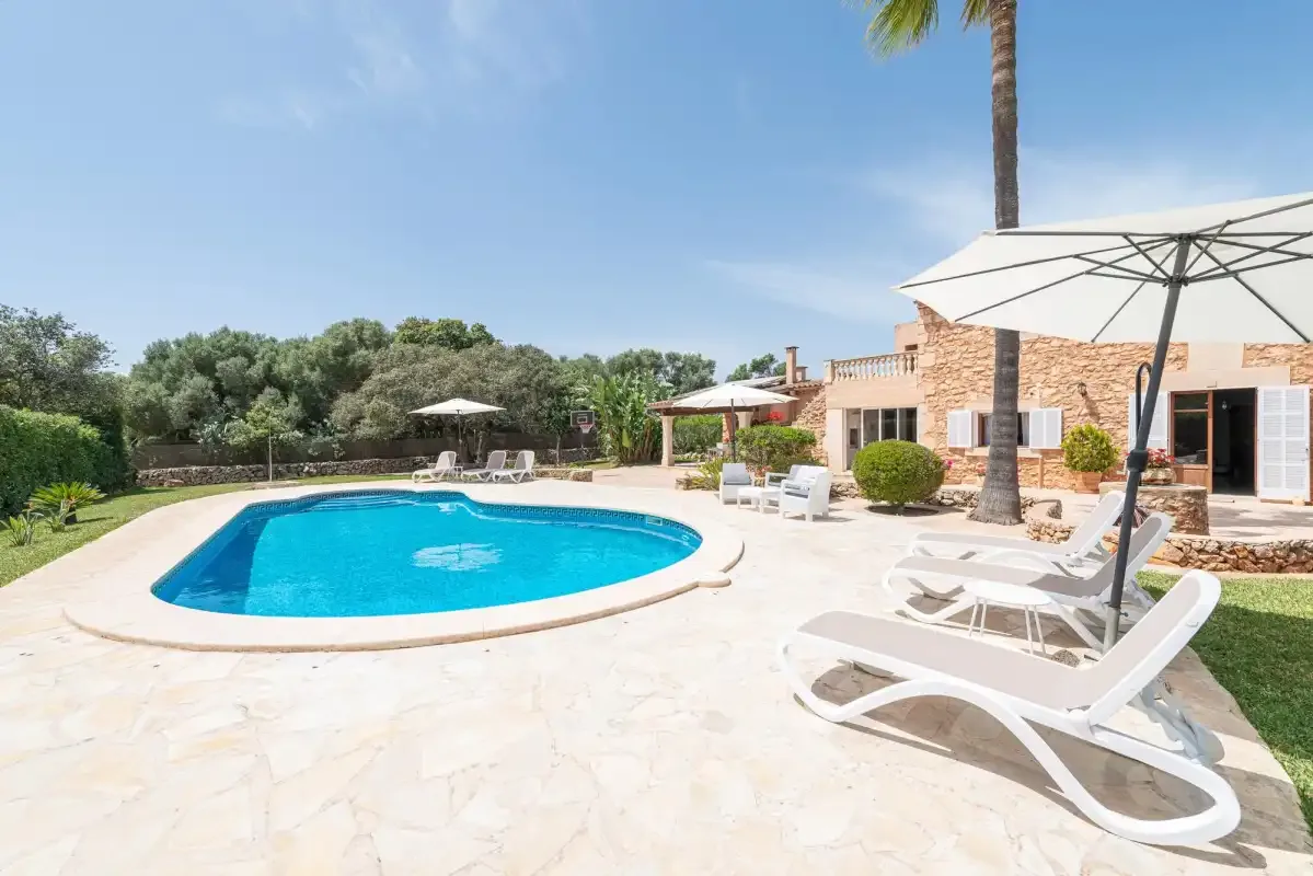 An outdoor swimming pool beside a patio with lounge seating and an umbrella.