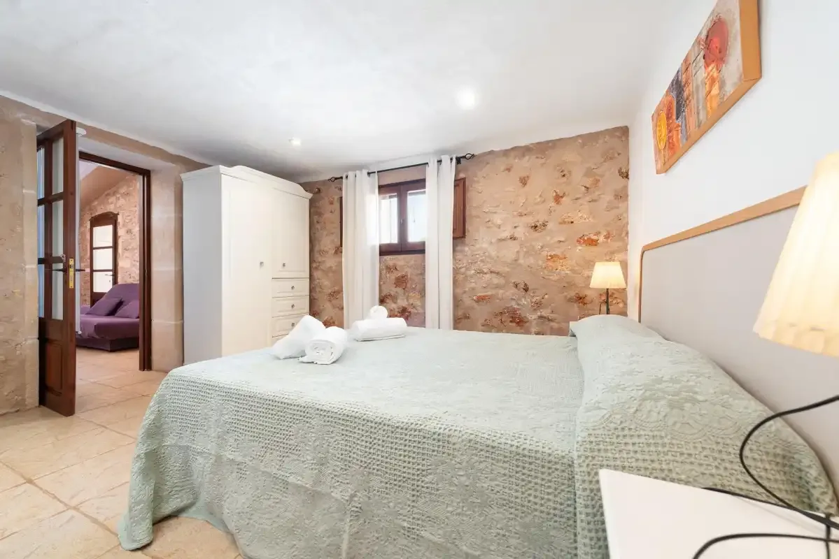A bedroom with a bed, white wardrobe, and exposed stone wall.