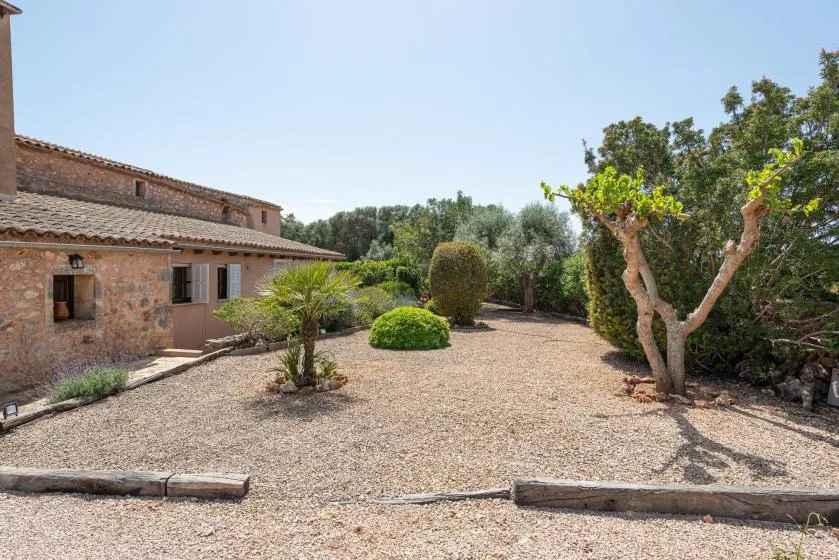 A gravel courtyard beside a stone building, with trees and shrubs.