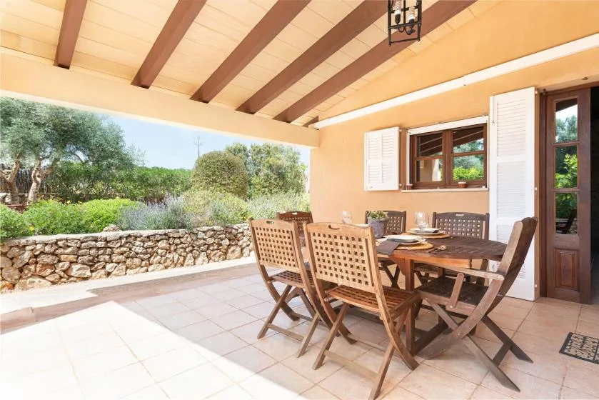 A covered patio with outdoor dining furniture overlooks a stone wall and garden.