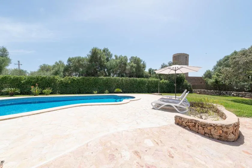 An outdoor swimming pool beside a sun umbrella and landscaped garden.