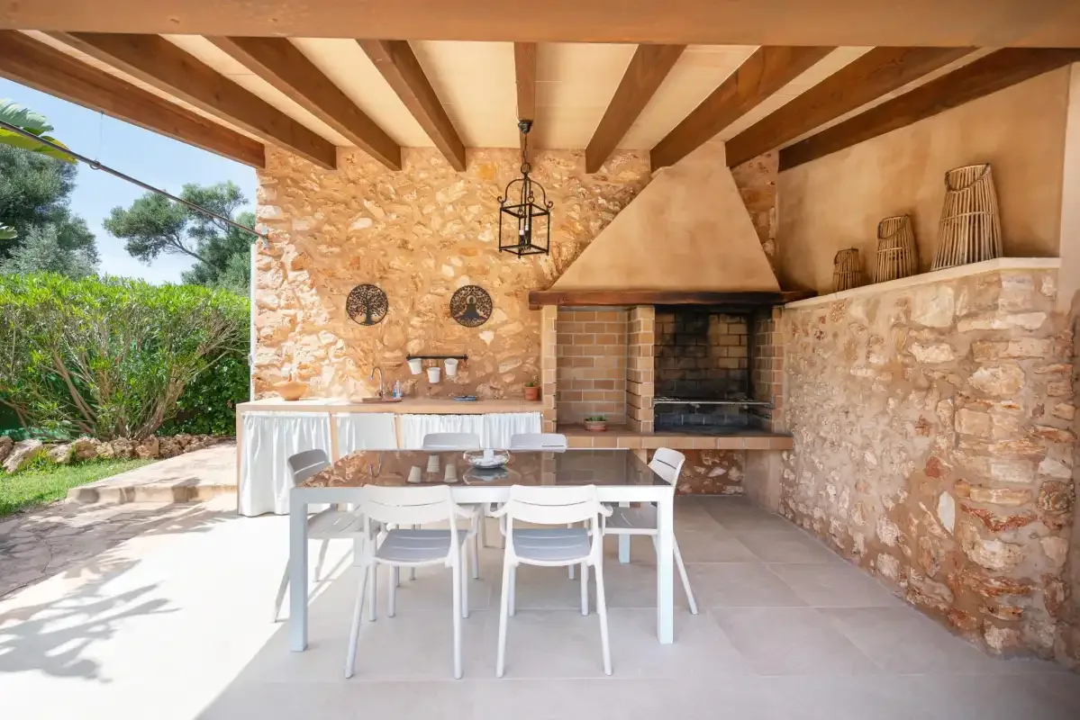 A covered outdoor dining area with a long table beside a stone barbecue.