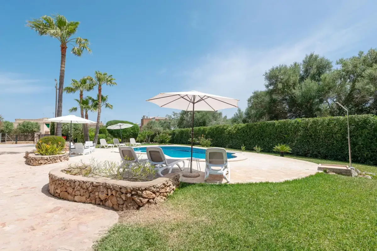 An outdoor pool area with patio seating, umbrellas, and surrounding greenery.
