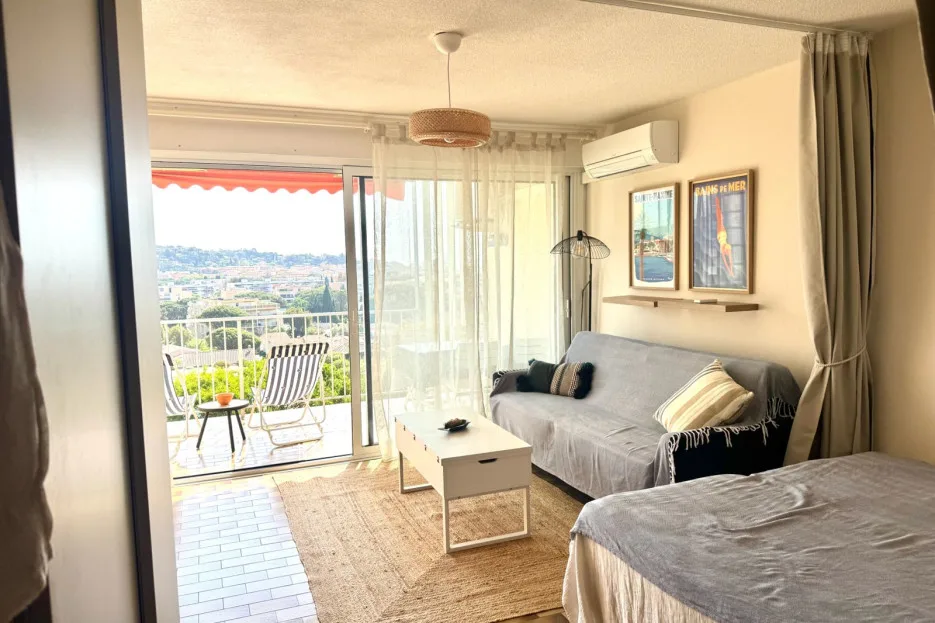 A bright bedroom with a bed, sofa, and sliding glass doors opening onto a balcony.