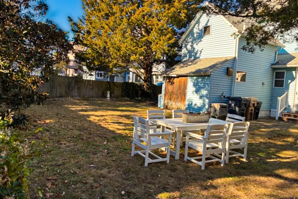 Un patio trasero con asientos blancos al aire libre junto a una casa azul.