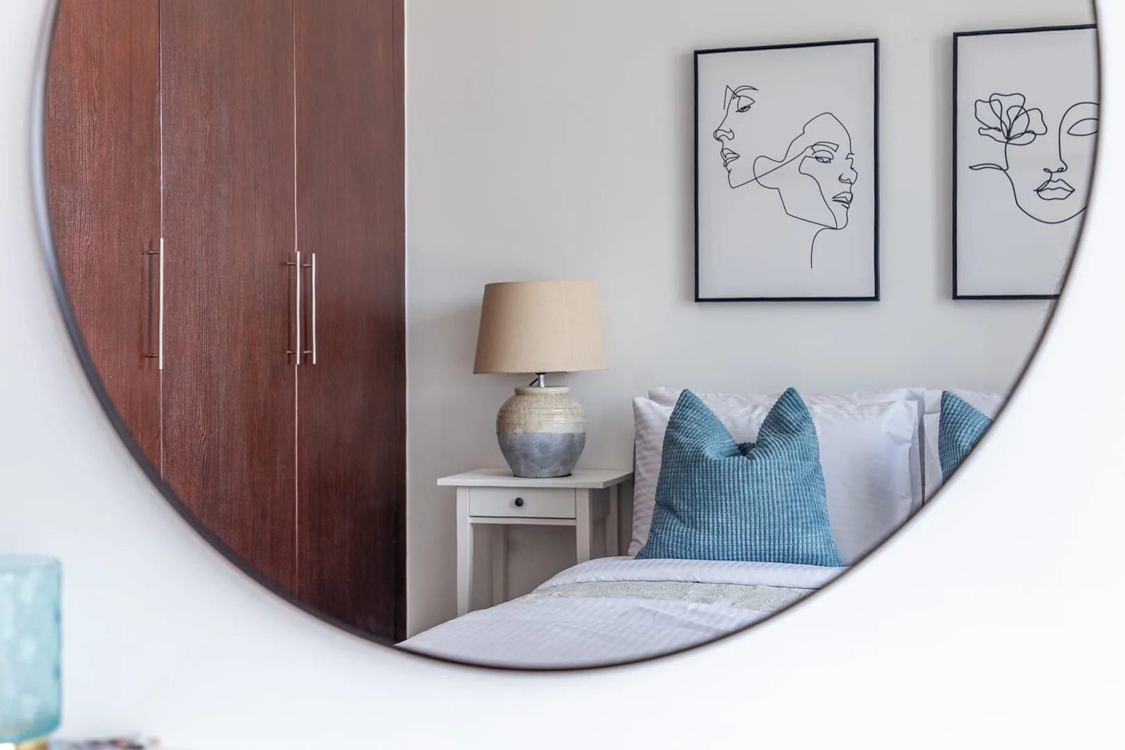 Un dormitorio reflejado en un espejo redondo, con una cama y una mesita de noche.