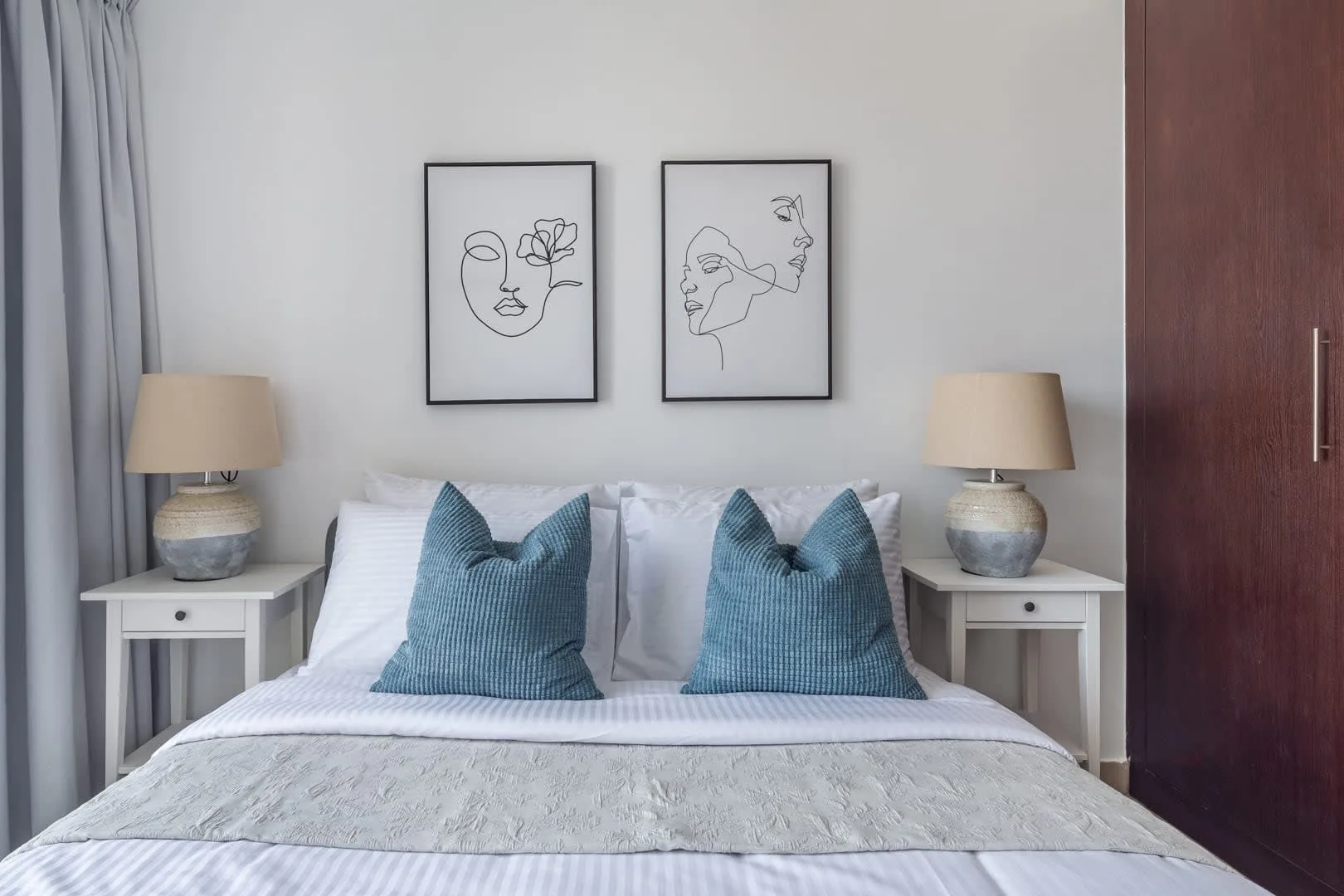 Un dormitorio con una cama bien tendida, cojines azules y lámparas a juego.