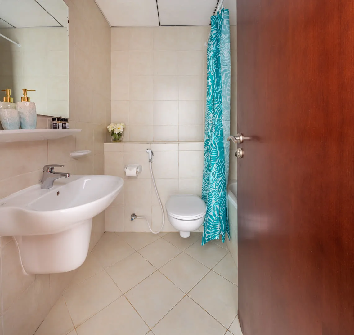 Un baño con azulejos, lavabo, inodoro y cortina de ducha turquesa.