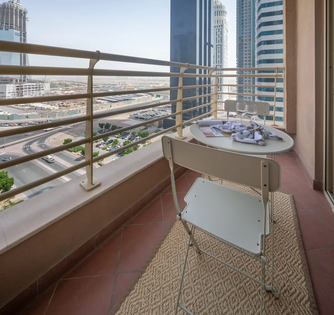 Una zona de estar en un balcón con una mesa pequeña y edificios de la ciudad al fondo.