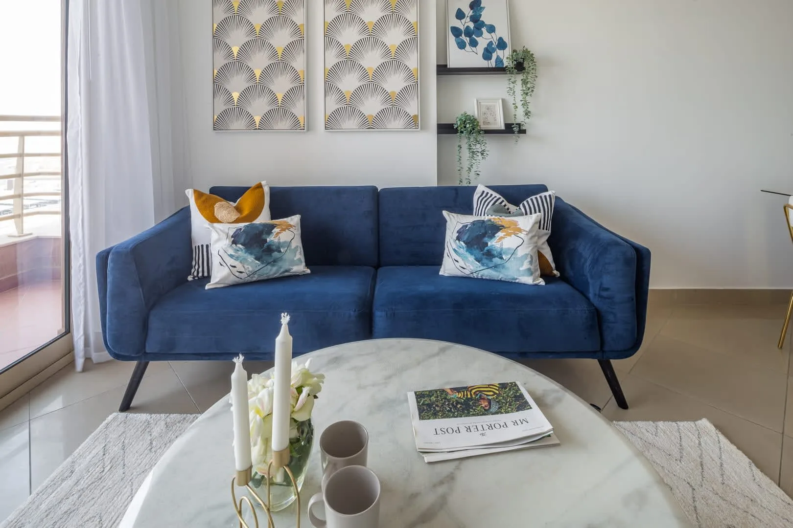 Una sala de estar con asientos azules, arte decorativo en la pared y una mesa de centro redonda.