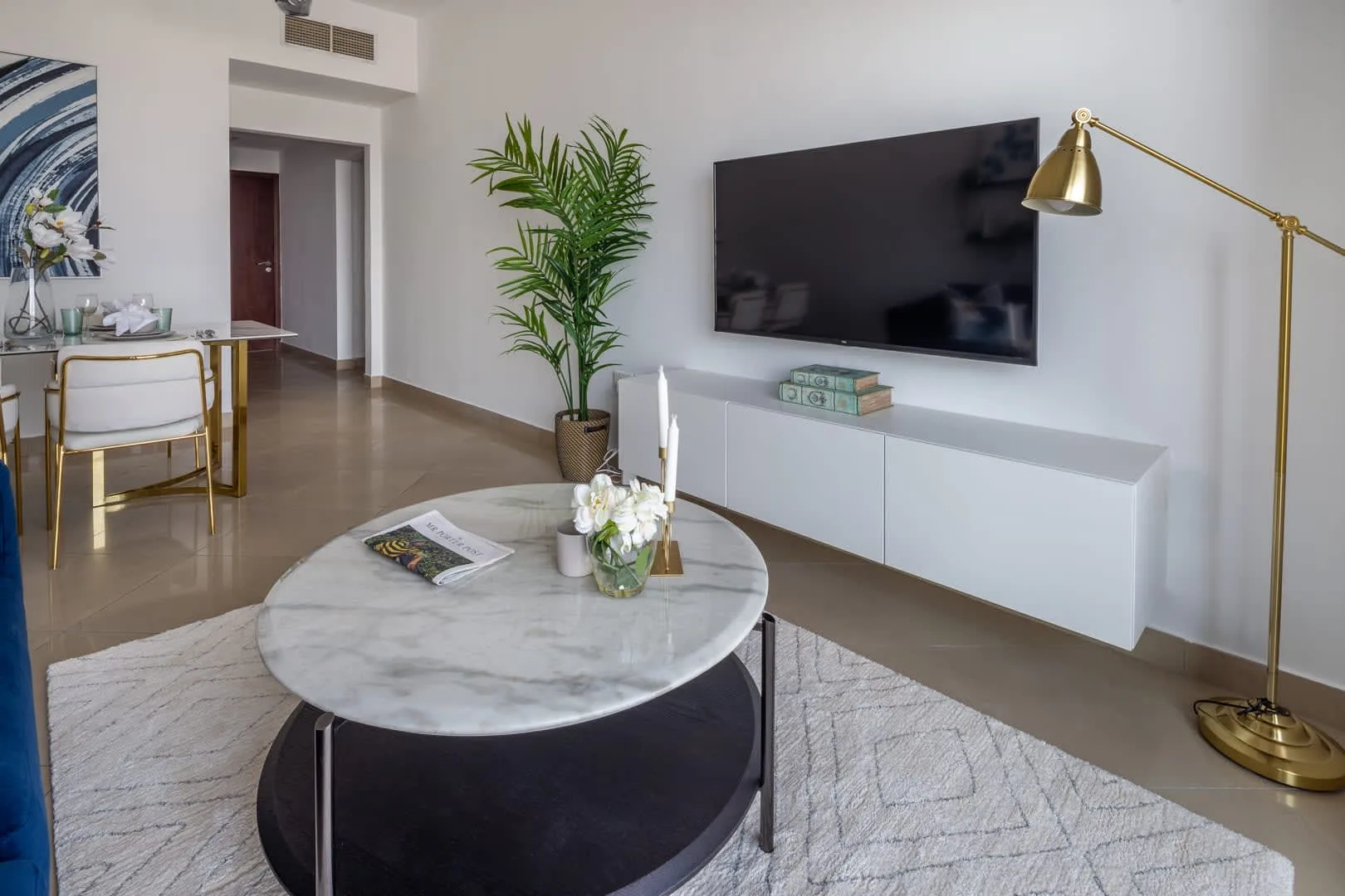 Una sala luminosa con mesa de centro redonda, televisor en la pared y lámpara de pie.