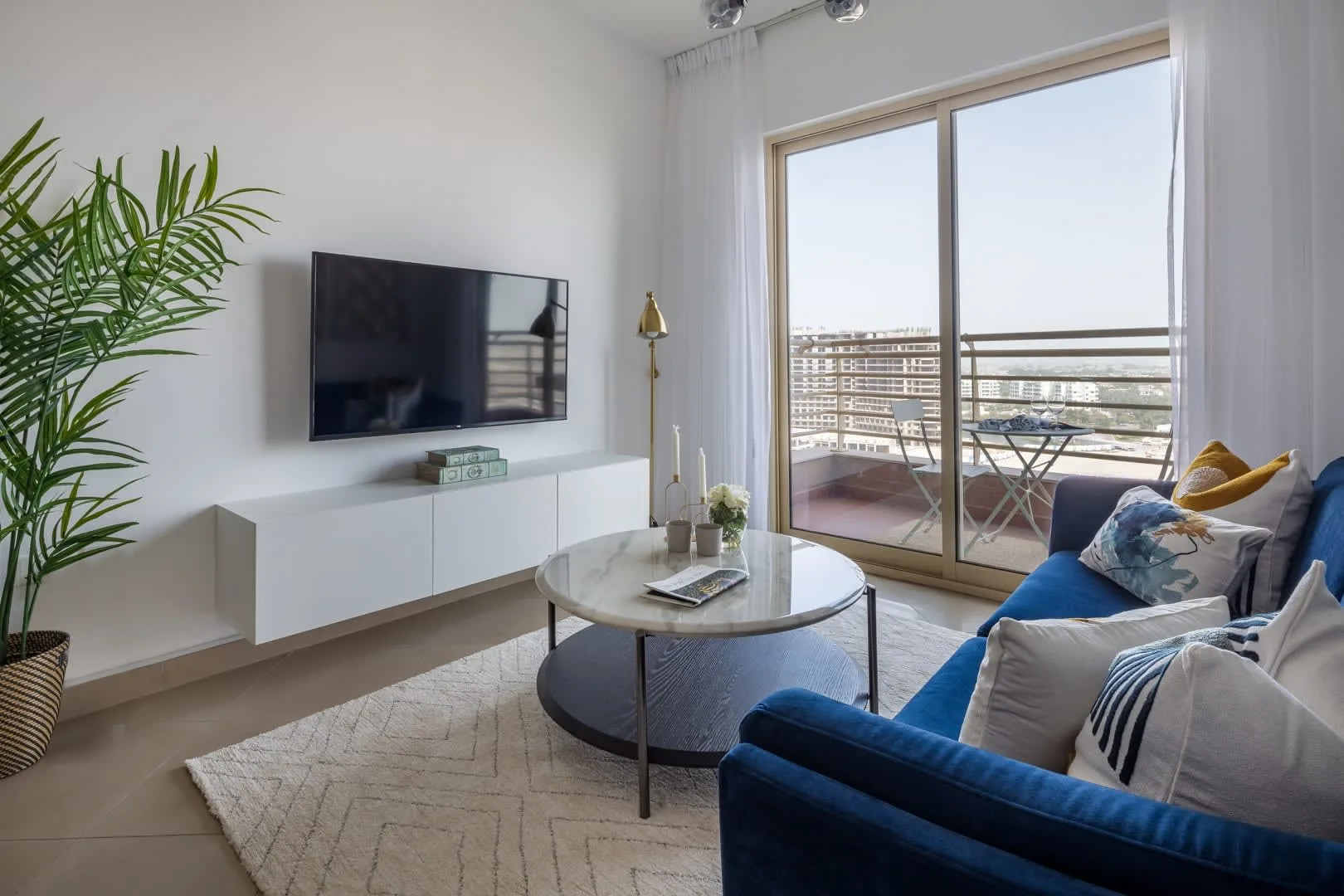Una sala luminosa con asientos azules, un televisor y puertas de vidrio que dan a un balcón.