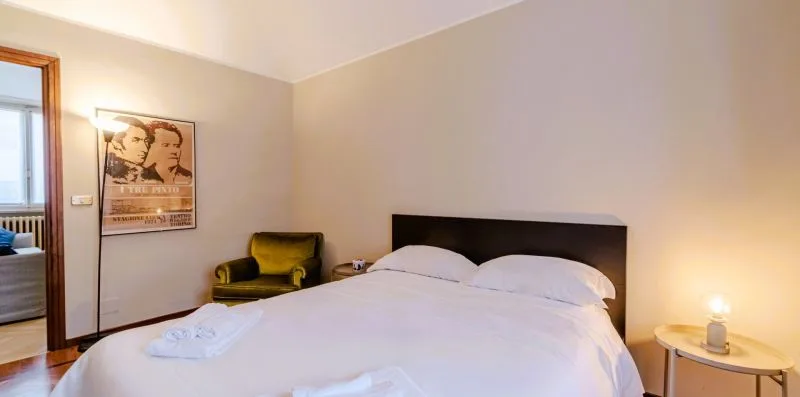 Un dormitorio con una cama tendida y un sillón junto a la pared.