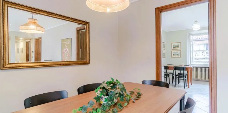 Un comedor con una mesa de madera, un centro de hojas y un espejo grande en la pared.