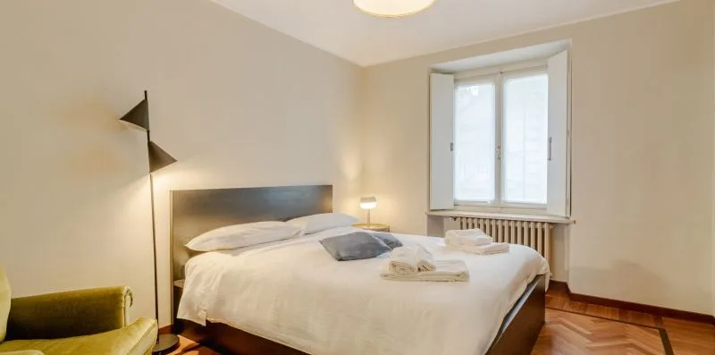 A bedroom with a neatly made bed and a window above a radiator.