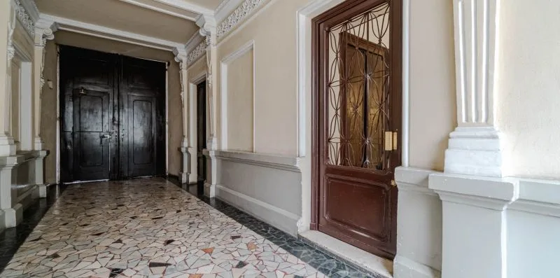 Un pasillo interior de baldosas con una puerta doble oscura al fondo.