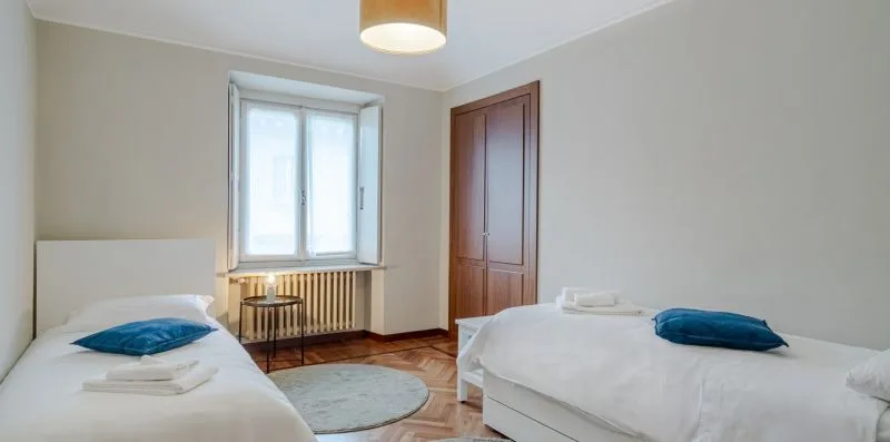 A bedroom with two beds, a window, and a small bedside table.
