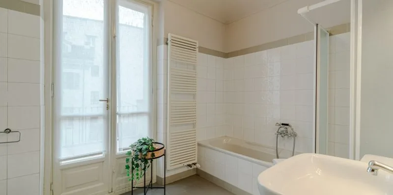 Un baño con azulejos, bañera, ventanas altas y un lavabo en primer plano.