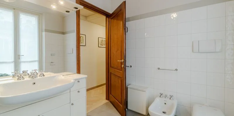Un baño alicatado con bañera, lavabo y una puerta de madera abierta.