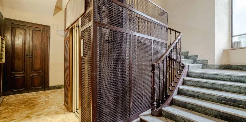 Una escalera interior con peldaños de piedra junto a una estructura metálica de ascensor.
