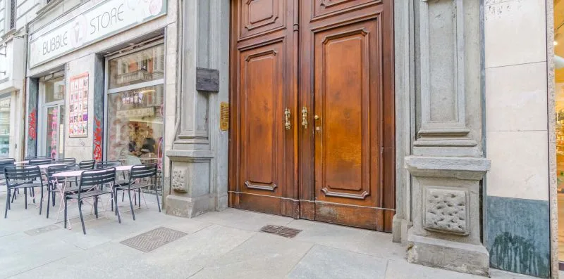 Un escaparate y una entrada de madera ornamentada dan a una acera pavimentada con mesas al aire libre.