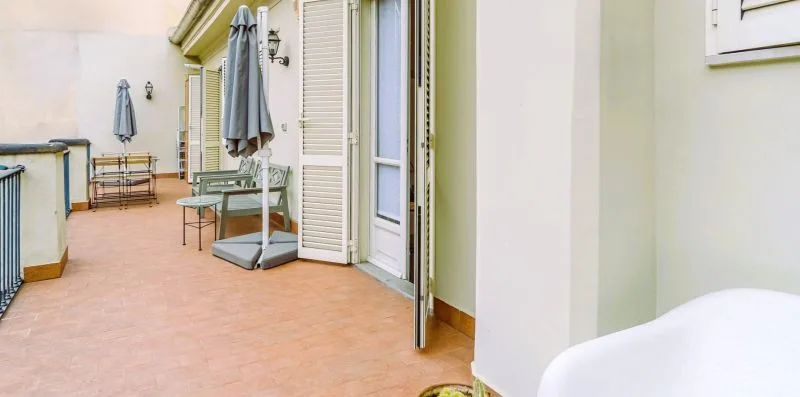 Una terraza embaldosada con asientos al aire libre y sombrillas plegadas junto a puertas abiertas.