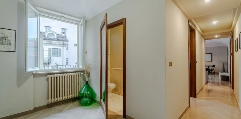 Un pasillo luminoso con una ventana grande y una puerta abierta al baño.