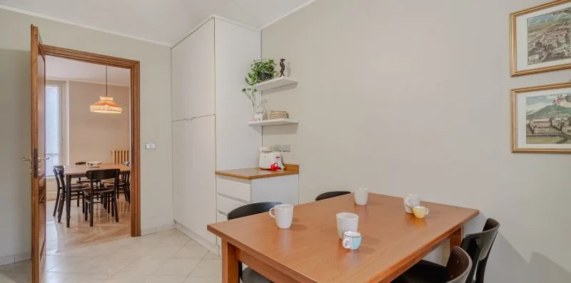 Un comedor con una mesa de madera, sillas y estantes en la pared.