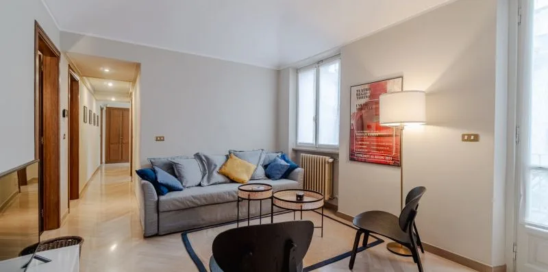 Una sala de estar con asientos, mesas bajas y una lámpara de pie junto a una ventana.