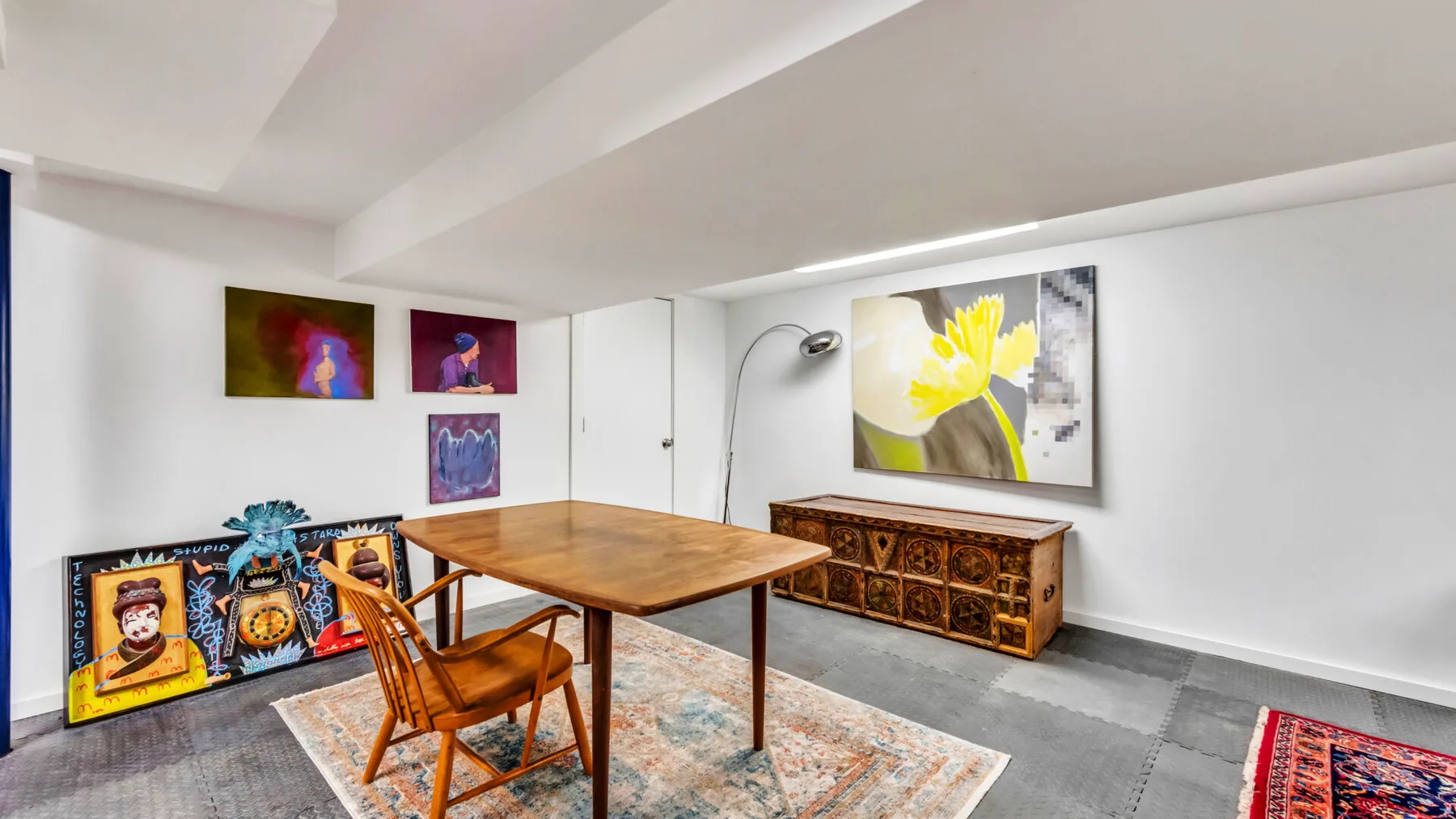 A bright living room with a wooden table, seating, and colorful artwork on the walls.