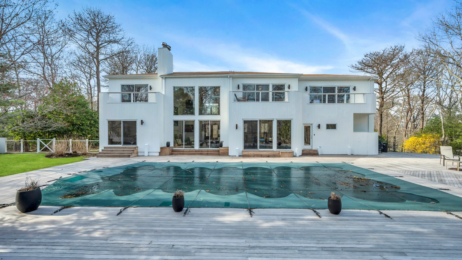 A white modern house overlooks a covered swimming pool and broad wooden deck.