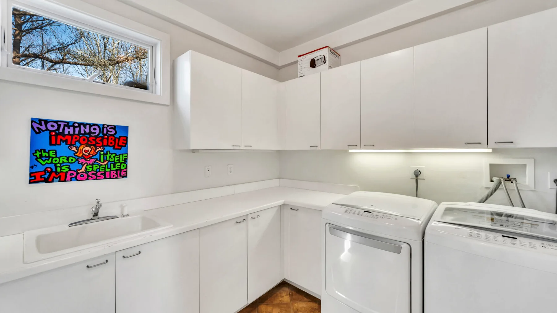 A bright laundry room with white cabinets, a sink, and laundry machines.