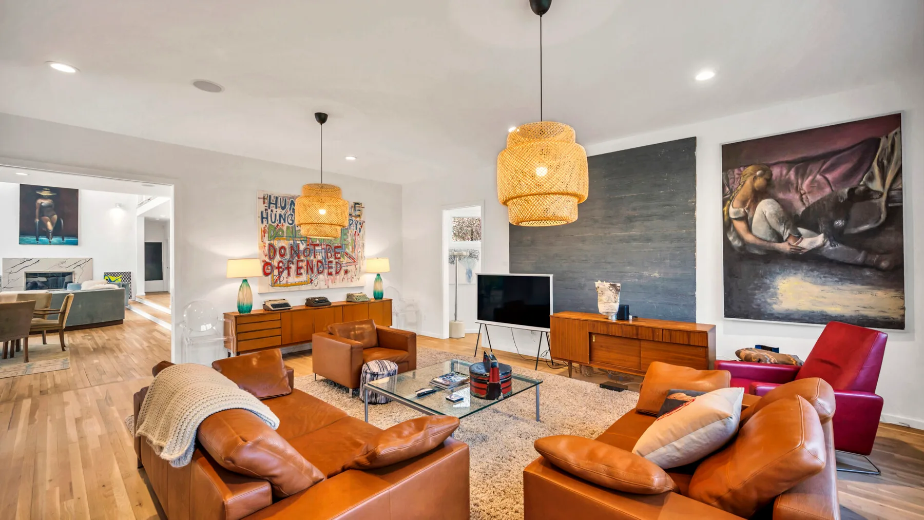 A bright living room with leather seating, a glass coffee table, and colorful wall art.