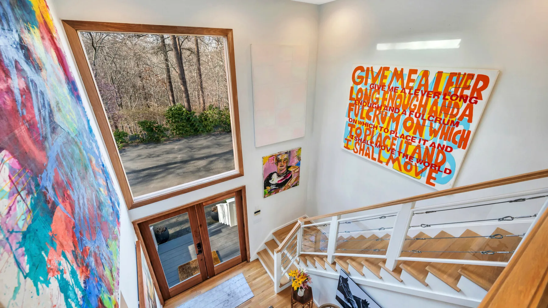 A bright stairwell with wooden steps, white railings, and colorful wall art.