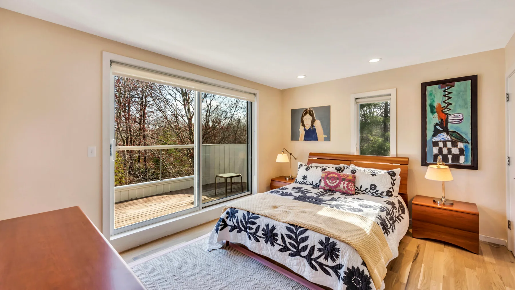 A bedroom with a bed beside large windows overlooking trees.